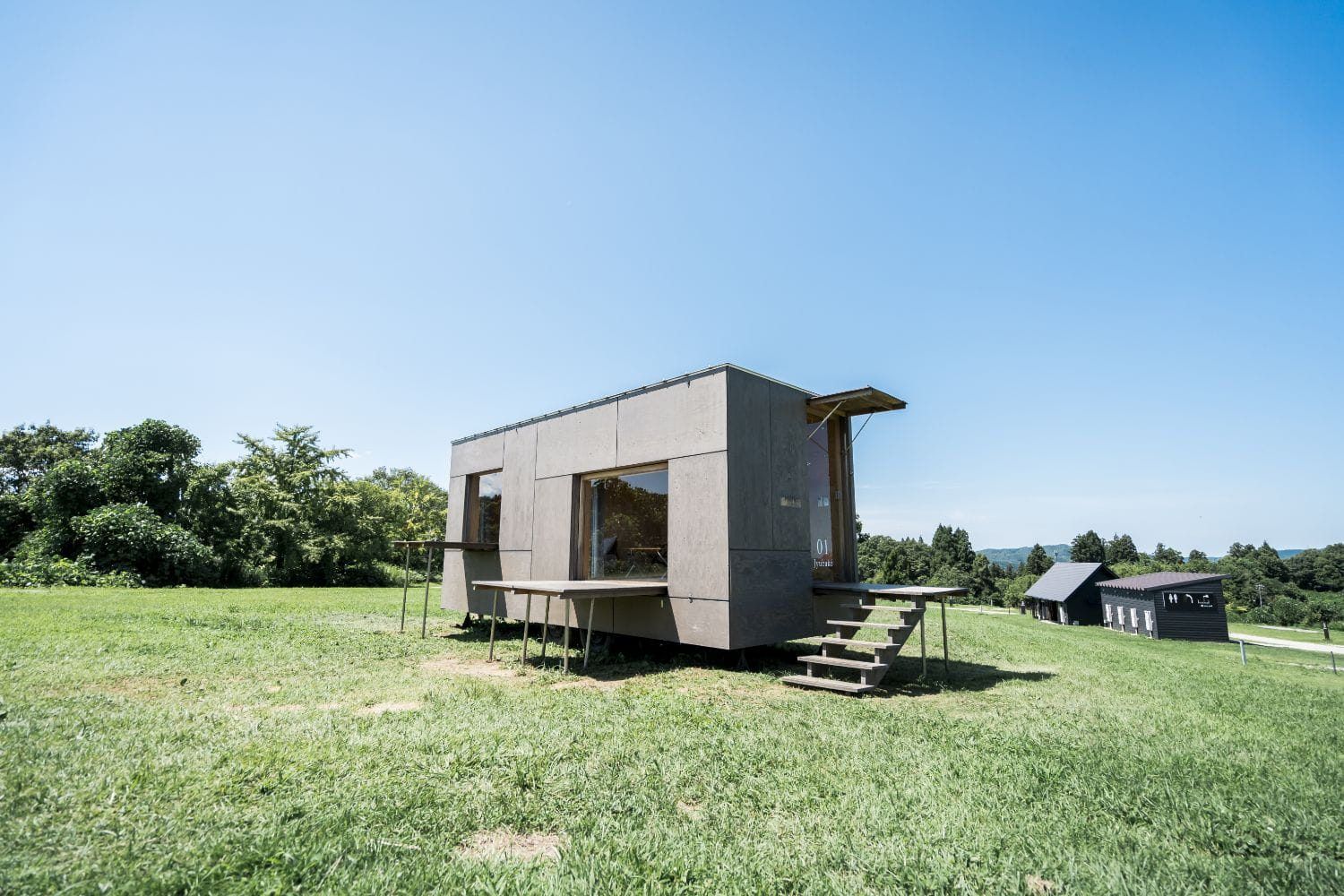 Ảnh 14 · JYUBAKO 住箱 phía campfield — mobile house Kengo Kuma đồng thiết kế, đặt trên chân thép, cửa kính lớn về phía đồi. Nguồn: snowpeak.co.jp